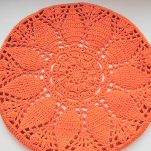 May include: A large, round, orange crochet doily with a detailed, intricate pattern.