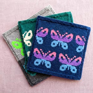 May include: Three square knitted coasters featuring butterfly patterns. The top coaster is dark blue with purple and light blue butterflies. The middle coaster is teal with white butterflies. The bottom coaster is gray with bright green butterflies.