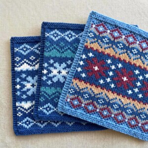 Può includere: Tre strofinacci quadrati lavorati a maglia con intricati motivi Fair Isle nelle tonalità del blu, verde acqua, bianco, marrone chiaro e bordeaux. Ogni panno presenta un design geometrico distinto con motivi ripetuti di fiocchi e rombi.