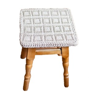 May include: A wooden stool with a crocheted cushion in a light beige color. The cushion has a square pattern.