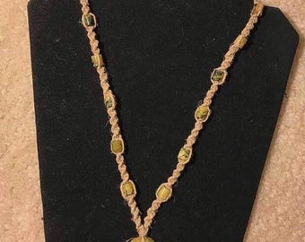 May include: A hemp necklace with a large green and brown stone pendant. The necklace is made with brown hemp cord and has small green and brown stone beads.