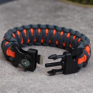 May include: A gray and orange paracord bracelet with a compass and a black plastic buckle.