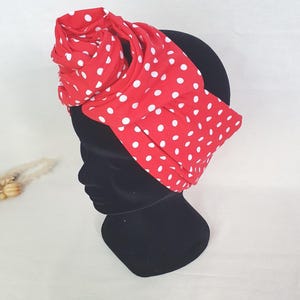 Peut inclure: Un turban rouge à pois blancs. Le tissu est rouge vif avec des pois blancs. Le turban est enroulé autour d'une tête de mannequin noire. Il est orné d'un grand nœud décoratif.