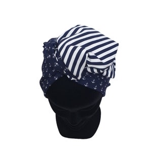 Puede incluir: Un sombrero de tem&aacute;tica n&aacute;utica con un dise&ntilde;o en capas. El sombrero presenta una tela azul marino con patrones de anclas blancas, una secci&oacute;n a rayas azul marino y blanco, y una base negra s&oacute;lida. El sombrero est&aacute; dise&ntilde;ado para ser usado en la cabeza.