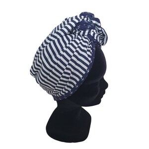 Puede incluir: Un turbante a rayas azul marino y blanco. La tela presenta un tema n&aacute;utico con dise&ntilde;os de anclas blancas en los bordes. El turbante se muestra en una cabeza de maniqu&iacute; negra.