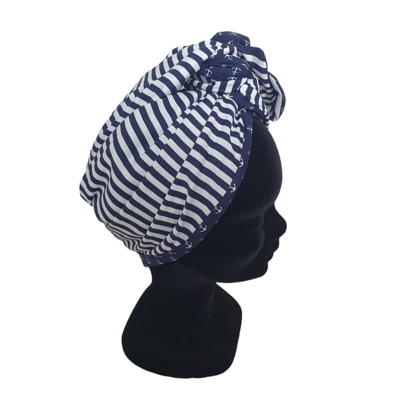 Puede incluir: Un turbante a rayas azul marino y blanco. La tela presenta un tema n&aacute;utico con dise&ntilde;os de anclas blancas en los bordes. El turbante se muestra en una cabeza de maniqu&iacute; negra.