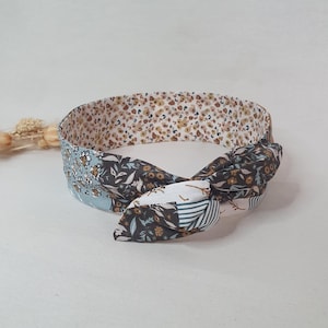 Peut inclure: Un bandeau pour les cheveux à motifs floraux avec un nœud. Le bandeau présente un mélange de motifs, notamment de petites fleurs, des feuilles et des rayures, dans des tons de bleu, marron, blanc et beige. Le bandeau est conçu pour être porté autour de la tête.