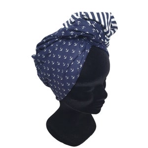 Puede incluir: Una diadema azul marino estilo turbante con tem&aacute;tica n&aacute;utica. La diadema presenta un patr&oacute;n de anclas blancas sobre un fondo azul marino, con una secci&oacute;n a rayas blancas y azul marino en la parte superior. La tela est&aacute; envuelta y anudada.