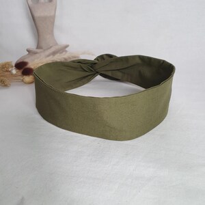 May include: Olive green knotted headband. The headband is made of a soft fabric and features a twisted knot design at the top. The headband is a solid color and is suitable for various hairstyles.