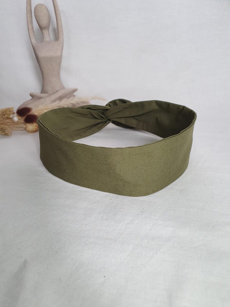 May include: Olive green knotted headband. The headband is made of a soft fabric and features a twisted knot design at the top. The headband is a solid color and is suitable for various hairstyles.
