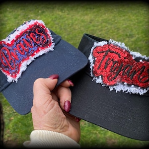 May include: Two black visor hats with white trim and red sequin patches. The patches say "Dames" and "Taggers".