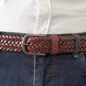 K&ouml;nnte beinhalten: Ein brauner geflochtener Lederg&uuml;rtel mit einer silbernen Schnalle. Der G&uuml;rtel wird &uuml;ber einer blauen Jeans getragen.