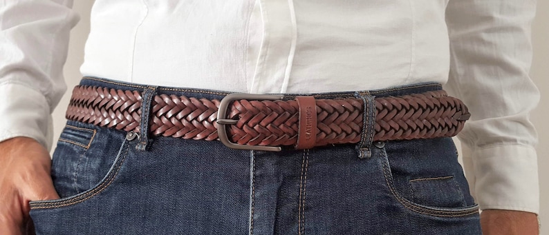 K&ouml;nnte beinhalten: Ein brauner geflochtener Lederg&uuml;rtel mit einer silbernen Schnalle. Der G&uuml;rtel wird &uuml;ber einer blauen Jeans getragen.