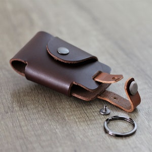 May include: A brown leather key holder with a snap closure and a metal key ring. The holder is open and the key ring is detached.