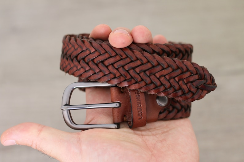K&ouml;nnte beinhalten: Ein brauner geflochtener Lederg&uuml;rtel mit einer silbernen Schnalle. Der G&uuml;rtel hat den Text "Leather" gepr&auml;gt.