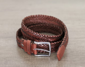 May include: A brown leather belt with a braided design and a silver buckle. The belt is rolled up and the buckle is visible. The text "Leather" is embossed on the belt.