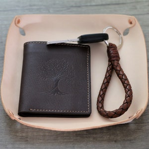 May include: A brown leather tray with a brown leather wallet and a brown leather key chain. The wallet has a tree design embossed on it.