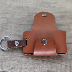 May include: A brown leather key holder with a metal ring and a snap closure. The key holder has a small pocket on the front.
