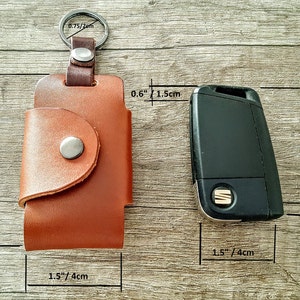May include: Brown leather key holder with a snap closure and a metal key ring. The key holder measures 3 inches by 1.5 inches. A black car key is shown next to the key holder for size comparison.