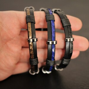 K&ouml;nnte beinhalten: Drei Lederarmb&auml;nder mit Metallakzenten. Die Armb&auml;nder sind schwarz, braun und blau.