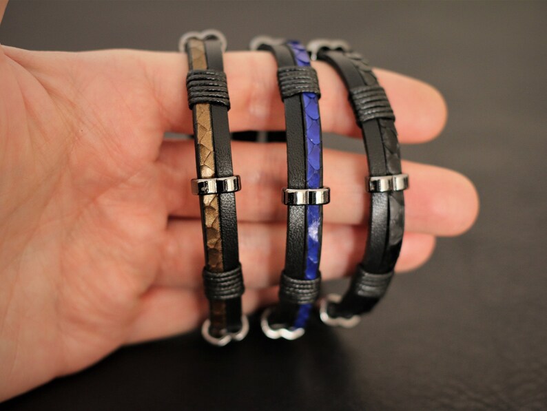 K&ouml;nnte beinhalten: Drei Lederarmb&auml;nder mit Metallakzenten. Die Armb&auml;nder sind schwarz, braun und blau.