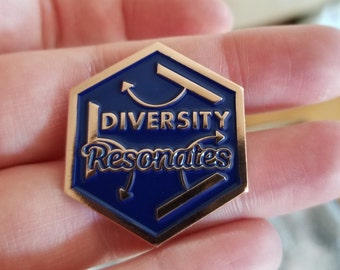 May include: A gold hexagonal pin with a blue enamel background. The pin features a stylized design of arrows pointing in different directions and the text "Diversity Resonates".