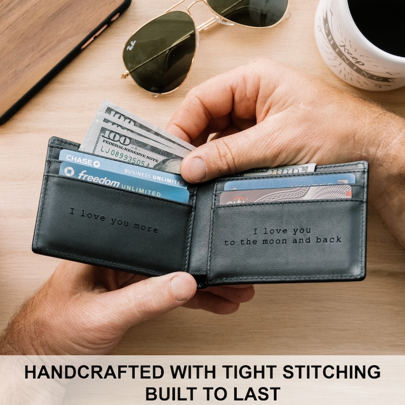 May include: A black leather wallet with a stitched design. The wallet is open and has cash and credit cards inside. The inside of the wallet is engraved with the text "I love you more" and "I love you to the moon and back".