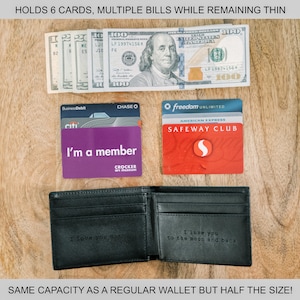 May include: A black leather wallet with a message engraved on the inside. The wallet is open and shows a cash bill, credit cards, and a membership card. The text on the wallet reads "I love you to the moon and back".