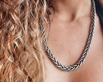 Puede incluir: Un collar de cadena trenzada de plata usado por una persona con cabello castaño rizado.