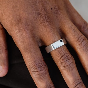 May include: A silver band ring with a black square inset on the top.