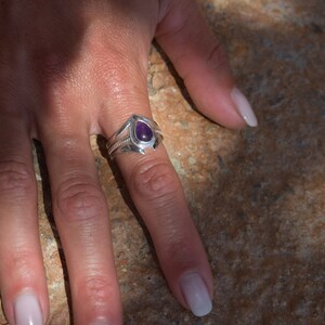 May include: A silver ring featuring a teardrop-shaped amethyst gemstone. The ring has a delicate design with a pointed tip and a twisted band.