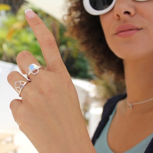 May include: Two silver rings on a finger. The ring on the top is a simple circle with a small opening in the center. The ring on the bottom is a geometric design with a pointed top.