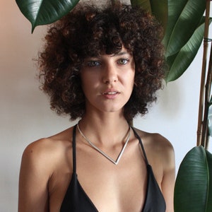 May include: A woman with curly brown hair wearing a black swimsuit top and a silver V-shaped choker necklace.