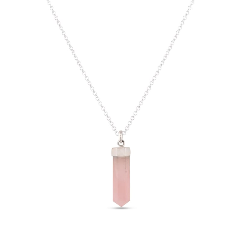 K&ouml;nnte beinhalten: Eine silberne Kettenkette mit einem rosa Kristall-Anh&auml;nger in Form einer Spitze.