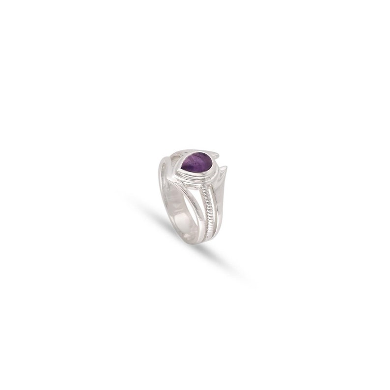 May include: A silver ring with a purple gemstone set in a heart-shaped design. The ring has a textured band.