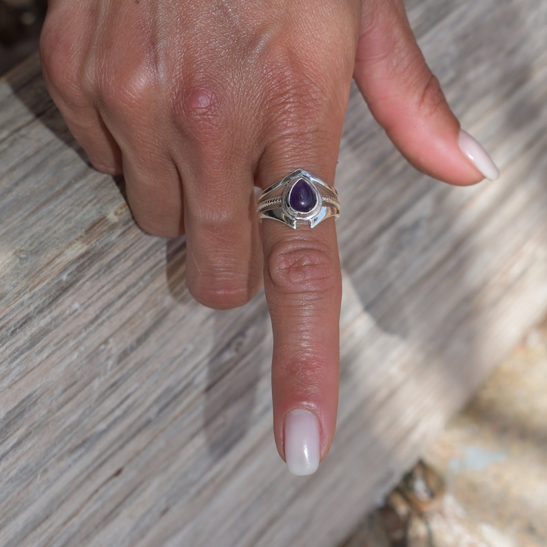 May include: A silver ring featuring a teardrop-shaped amethyst gemstone set in a delicate, ornate design.