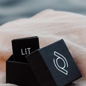 May include: A black box with a white logo on the lid. The box is open and a black card with the word "LIT" printed in white is inside.
