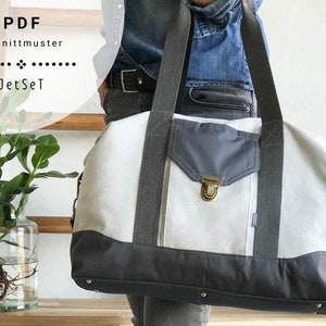 May include: A white and grey canvas duffel bag with a large front pocket and a brass clasp. The bag has a black strap and is being held by a person wearing jeans.