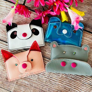 May include: Four small fabric pouches with animal faces. The pouches are in the shapes of a panda, a hippopotamus, a pig, and a blue whale. The pouches are all different colors and have different features, such as buttons, rhinestones, and embroidered details.