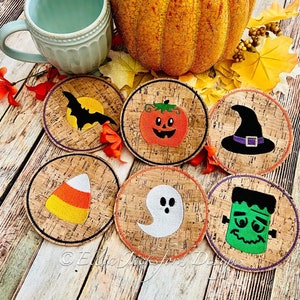 以下が含まれることがあります： ハロウィンをテーマにした刺繍のデザインが施された、丸いコルクコースターが6つ。デザインには、コウモリ、カボチャ、魔女の帽子、キャンディーコーン、幽霊、フランケンシュタインなどが含まれています。コースターは、カボチャとマグカップを背景に、木製の表面に配置されています。
