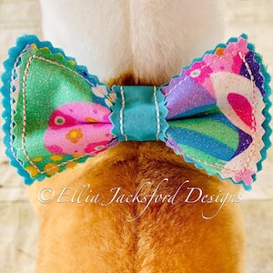 May include: A turquoise bow tie with a colourful floral pattern. The bow tie is made of fabric and has a scalloped edge. The bow tie is tied around the neck of a dog.