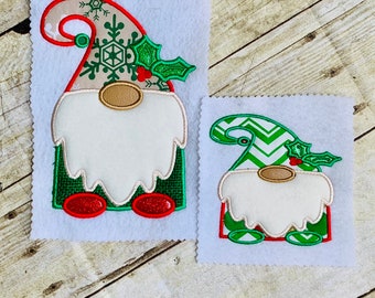 May include: Two felt Christmas gnome ornaments. The larger gnome has a brown hat with a snowflake and holly design. The smaller gnome has a green and white chevron hat with holly. Both gnomes have white beards, red shoes, and green bodies.