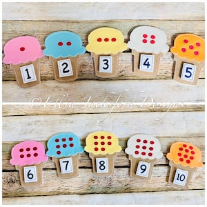 Może przedstawiać: Zestaw dziesięciu filcowych kształtów rożków lodów, każdy z innym kolorowym smakiem i numerem od jednego do dziesięciu. Smaki są różowe, niebieskie, żółte, białe i pomarańczowe, z czerwonymi kropkami. Wafelki są beżowe.