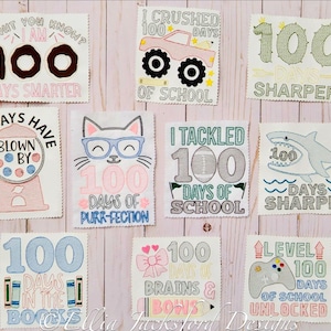 May include: Nine colorful embroidered patches with different designs and text celebrating 100 days of school. The patches feature a donut, a gumball machine, a cat, a monster truck, a shark, a video game controller, a book stack, and a bow. The text on the patches includes "100 days smarter", "100 days of purr-fection", "100 days sharper", "100 days of school", "100 days in the books", "100 days unlocked", and "100 brains & bows".