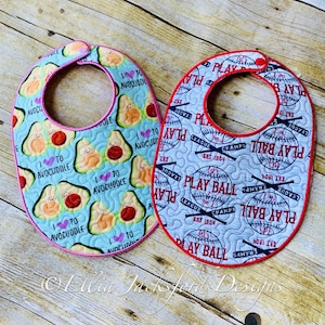 May include: Two baby bibs, one with a blue background and avocado designs with the text "I love to avocuddle", and the other with a white background and baseball designs with the text "Play Ball".