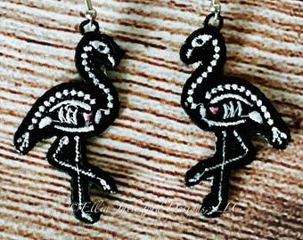 May include: A pair of black and white skeleton flamingo earrings with silver hooks. The earrings are made of felt and are approximately 2 inches tall.