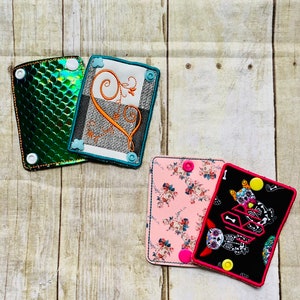 May include: Four different fabric patches with embroidered designs. The patches are rectangular and have a variety of colors and patterns, including green, blue, white, black, pink, and orange. The patches have a scalloped edge and are decorated with buttons.