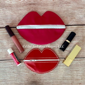 May include: Two red heart-shaped zippered pouches with white stitching. The pouch on the left has a white zipper and the pouch on the right has a red zipper. The pouches are on a wooden surface with a lip balm, lipstick, and a makeup brush.