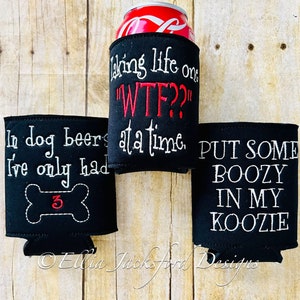 May include: Three black neoprene can coolers with white and red embroidered text. The first cooler says "In dog beers I've only had 3" with a white embroidered bone and the number 3 in red. The second cooler says "Taking life one "WTF?" at a time." The third cooler says "Put some boozy in my koozie."
