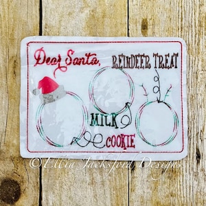 May include: White felt Christmas stocking with red trim and a Santa hat. The stocking has a red and green reindeer treat design with the words "Dear Santa, Reindeer Treat" and "Milk & Cookie" written on it.